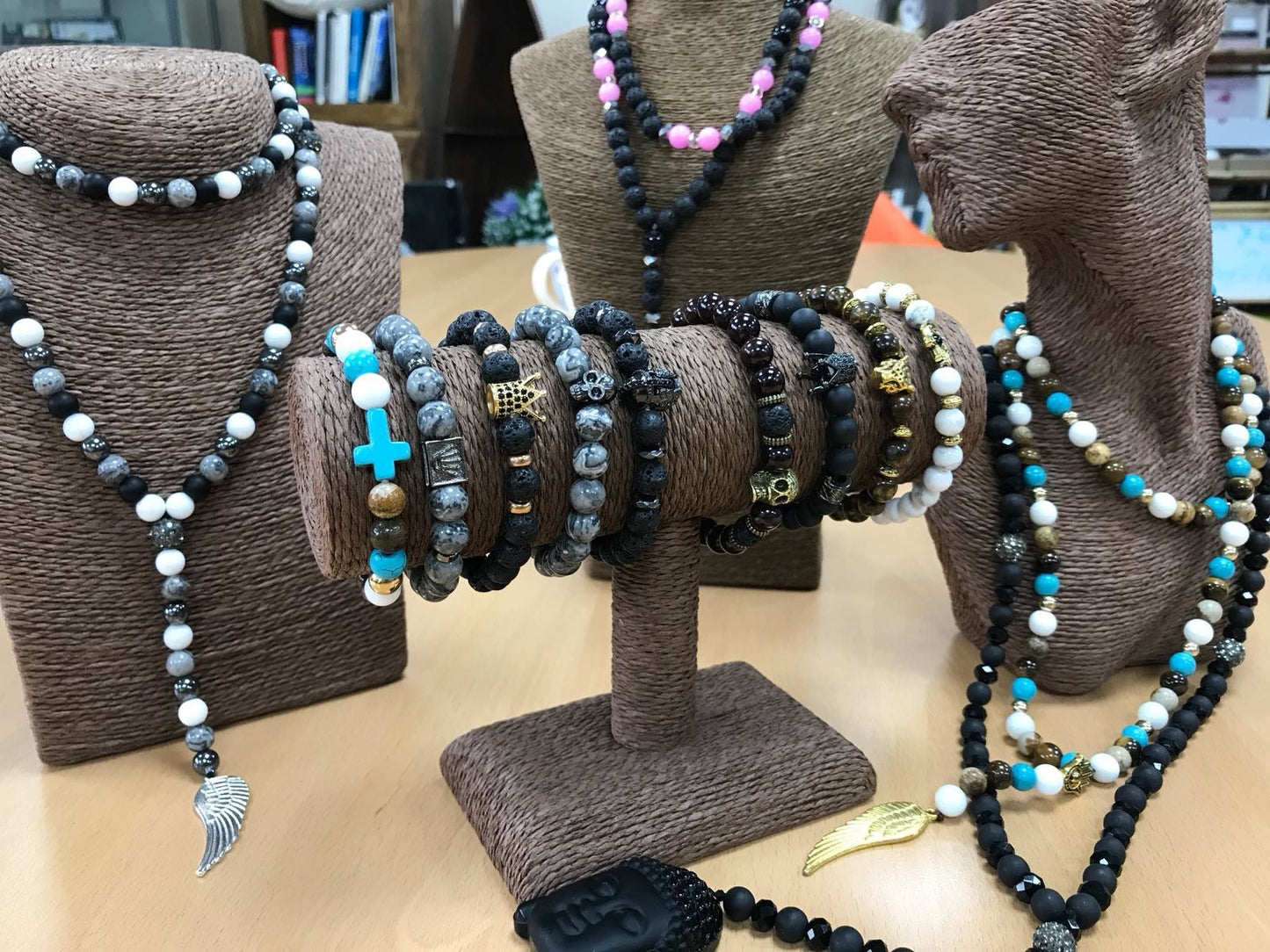 Collection of beaded necklaces on brown textured stands with a blurred indoor background.