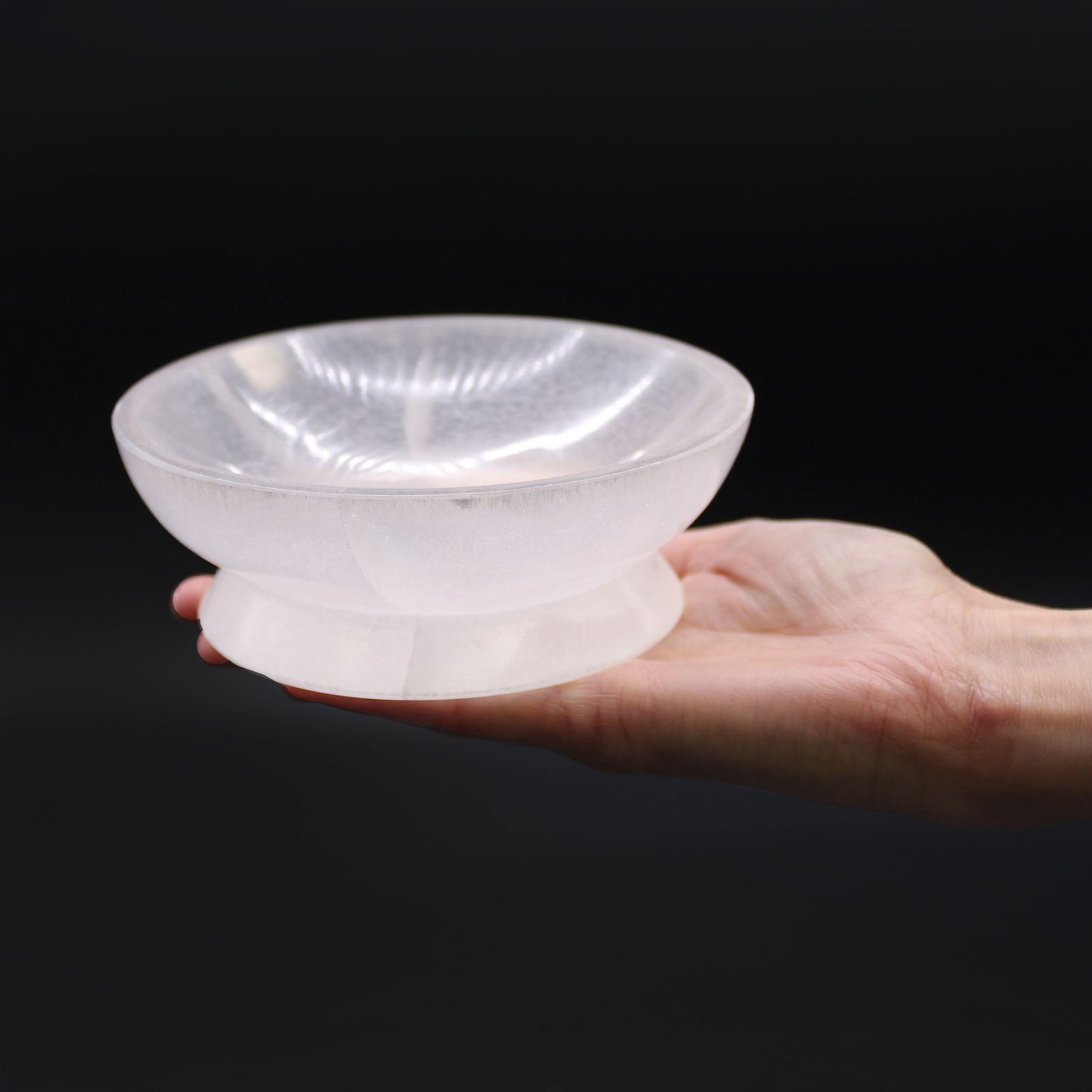 Hand holding a translucent white stone bowl against a black background