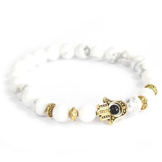 White beaded bracelet with gold and black hamsa hand charm on a white background